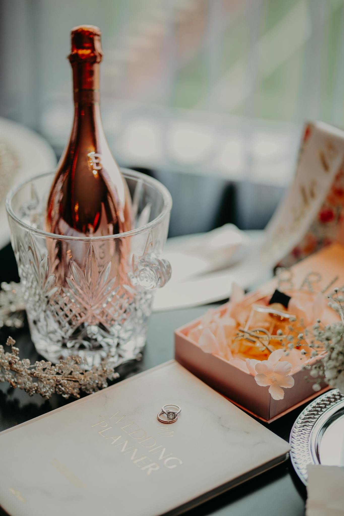 An elegant setup featuring a champagne bottle, crystal glassware, and a wedding planner with a ring, perfect for engagement celebrations.