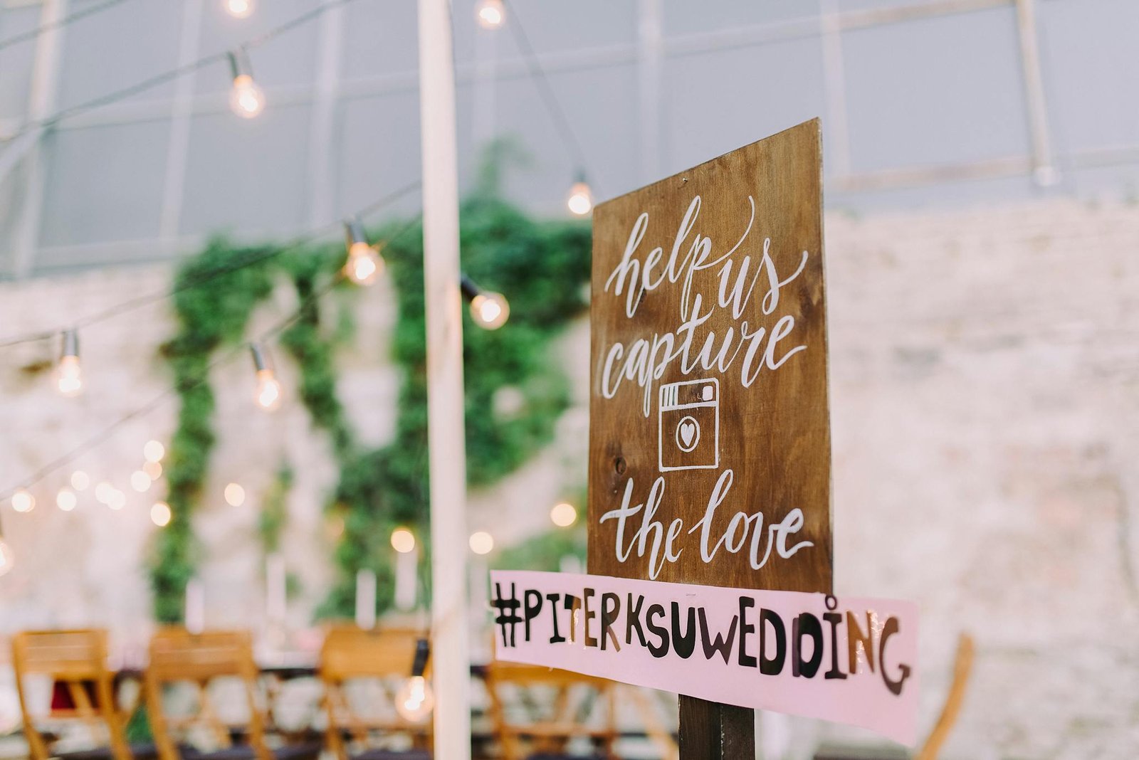 Charming outdoor wedding setup featuring rustic wooden signage with string lights in a romantic evening atmosphere.