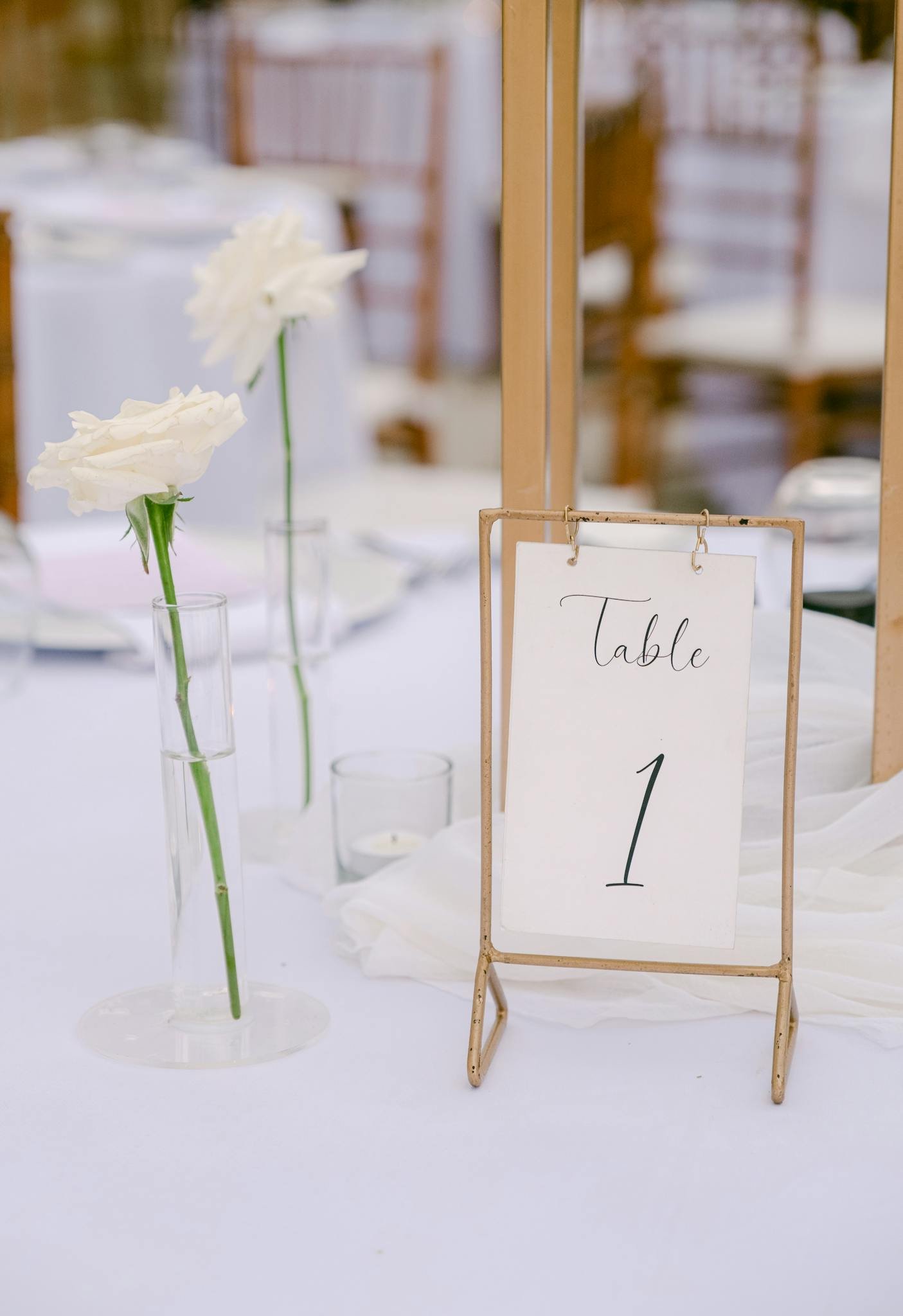 Elegant wedding table number setup with white flowers in glass vases.