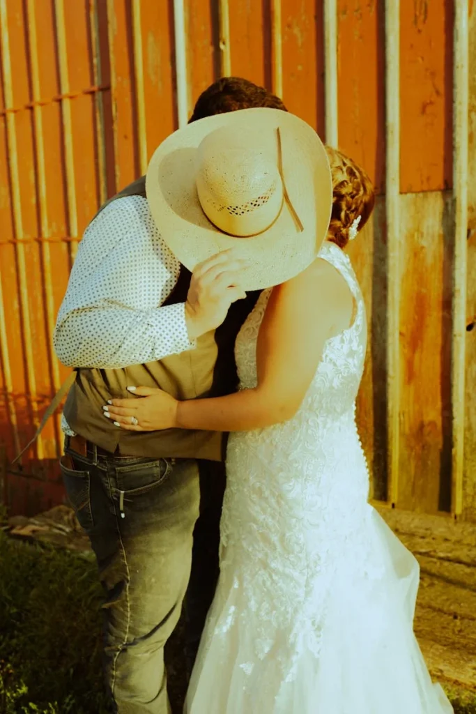 bride & groom kissing behind a cowboy hat